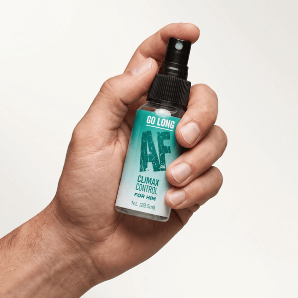 Man's hand holding the Go Long AF Delay Spray bottle with black spray nozzle and teal label
