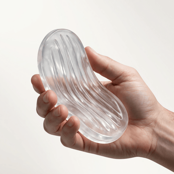 A hand holding a clear, textured Screaming O Jackits Stroker Pad against a plain background.