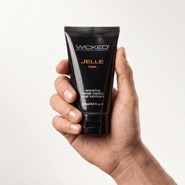 Hand holding a black tube of Wicked Jelle Heat Warming Anal Lube with orange lettering, 4 oz
