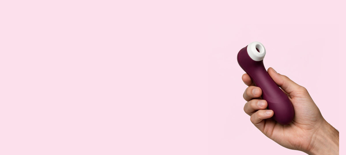A hand holding a wine red Satisfyer Pro 2 air pulse vibrator against a plain background.