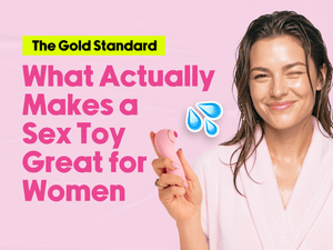 A woman smiling in na pink robe holds a pink vibrator next to text that reads, 'The Gold Standard: What Actually Makes a Sex Toy Great for Women'