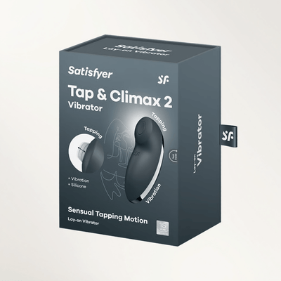 A hand holding a dark gray Satisfyer Tap & Climax 2 vibrator against a plain background.