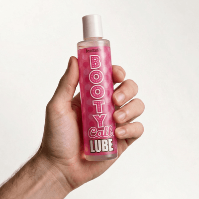 A hand holding a bottle of pink Booty Call Lube against a white background.