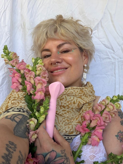 Person holding pink flowers and a pink Queenie V toy against a white background