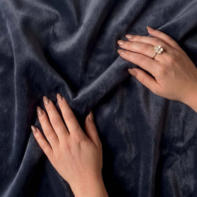 Hands touching charcoal fabric with a floral ring on one finger