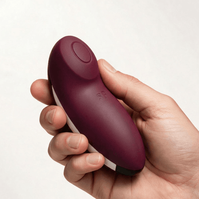 Hand holding the Satisfyer Tap & Climax 2 Lay-On Vibrator in dark red, showing rounded silicone body