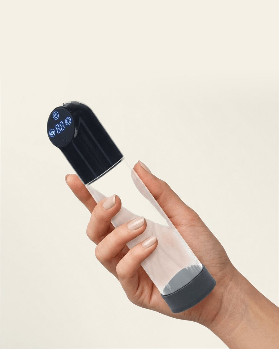 A hand holding the PUMPED automatic penis pump against a plain cream background