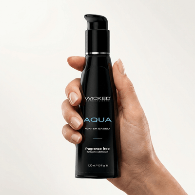 Hand holding a 4 oz bottle of Wicked Aqua Water Based Lube fragrance free against cream background